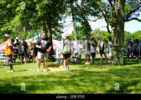 I maschi e le femmine giocano un gioco di lancio di sacco di fagioli all'evento del fine settimana di Walleye al parco del lago, come una comunità si riuniscono. Foto Stock