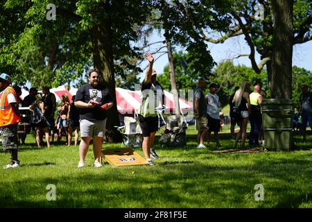 I maschi e le femmine giocano un gioco di lancio di sacco di fagioli all'evento del fine settimana di Walleye al parco del lago, come una comunità si riuniscono. Foto Stock