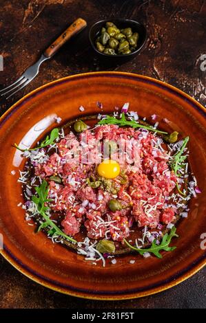 Tartare di bistecca di manzo con tuorlo d'uovo crudo, capperi sottaceto e parmigiano. Sfondo scuro. Vista dall'alto Foto Stock