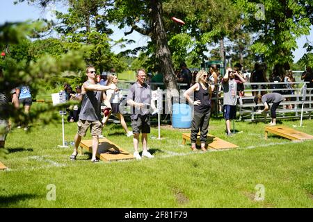 I maschi e le femmine giocano un gioco di lancio di sacco di fagioli all'evento del fine settimana di Walleye al parco del lago, come una comunità si riuniscono. Foto Stock