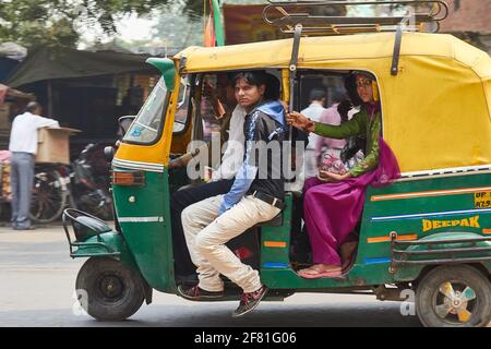 Due passeggeri che guardano verso la macchina fotografica da un affollato giallo e verde auto rickshaw indiano ad Agra, India Foto Stock