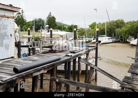 Yeppoon, Queensland, Australia - Aprile 2021: Un vecchio molo di legno su un torrente costiero con barche ormeggiate a bassa marea Foto Stock