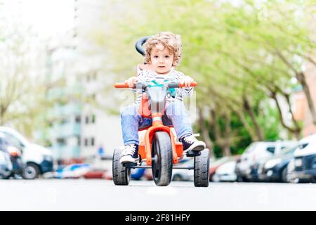 Ragazzo di due anni e mezzo seduto su di lui triciclo sulla strada in mezzo alla strada Foto Stock