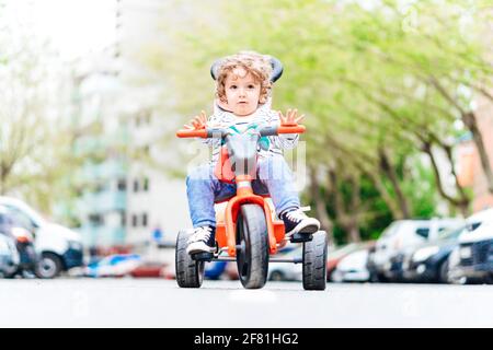 Ragazzo di due anni e mezzo seduto su di lui triciclo sulla strada in mezzo alla strada Foto Stock