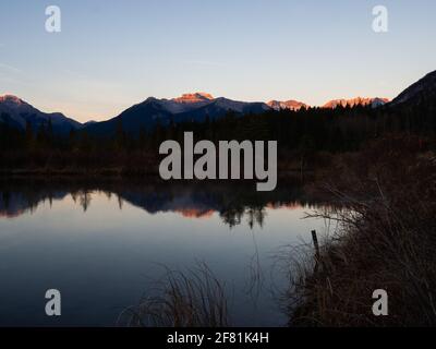 lago calmo che rispecchia le montagne dietro in estate su un alba o tramonto Foto Stock