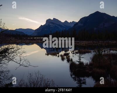 lago calmo al mattino che riflette un'alta montagna alle spalle durante l'ora blu in estate Foto Stock