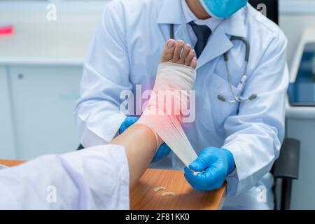 Close-up mano di medico ortopedico indossare guanti medici di medico mano legatura bendaggio sulla gamba del paziente in clinica, osteofiti e tallone, infiammati Foto Stock