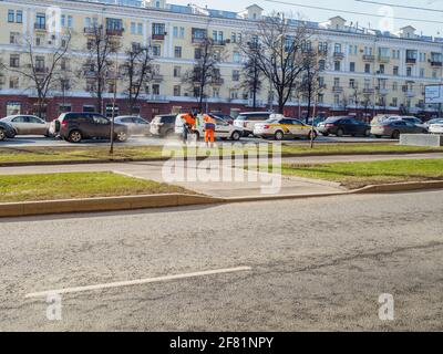 Mosca. Russia. 06 aprile 2021. Gianti in uniforme arancione che spazzano il prato lungo una strada in una strada cittadina. Giorno di primavera soleggiato. Il lavoro del comune Foto Stock