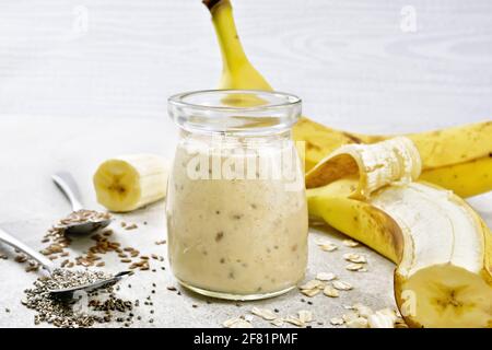 Frullato di latte con semi di chia, semi di lino, farinata d'avena, riso soffiato e banana in un vaso di vetro su uno sfondo di un tavolo di pietra Foto Stock