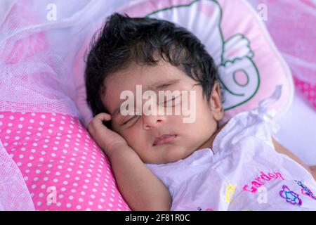 Bambina carina di 1 mese che dorme in un soffice cuscino rosa, nato con un sacco di capelli neri. Napping e sognare tempo per l'adorabile bambino sano. Foto Stock