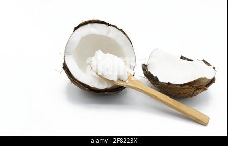 Concetto di cibo sano, un cucchiaio di legno con olio di cocco allo stato solido accanto a un cocco dimezzato su sfondo bianco Foto Stock