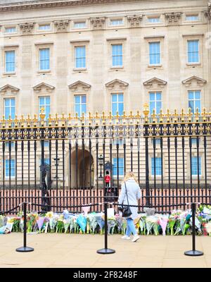 Buckingham Palace, Londra. Un membro del pubblico che pone un tributo floreale al Principe Filippo con la Guardia del Queens in piedi Sentry, Londra, Regno Unito, 2 aprile Foto Stock