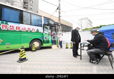 Pechino, Cina. 11 Apr 2021. I lavoratori della Comunità compilano una scheda di osservazione per un uomo dopo aver ricevuto un vaccino COVID-19 al di fuori di un veicolo di vaccinazione mobile nel distretto di Haidian a Pechino, capitale della Cina, il 11 aprile 2021. Pechino e Shanghai hanno implementato veicoli di vaccinazione mobili nelle aree del centro. Le strutture simili agli autobus, dotate di stazioni di vaccinazione, frigoriferi medici e attrezzature di pronto soccorso, sono state introdotte per risparmiare tempo e migliorare l'efficienza dell'inoculazione. Credit: Ren Chao/Xinhua/Alamy Live News Foto Stock