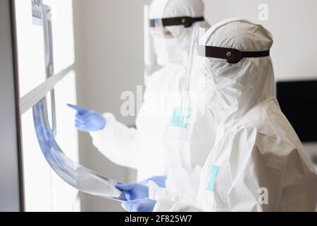 Due medici in tute protettive e maschere esaminano un radiografia Foto Stock