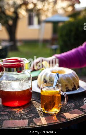 Tazza da tè e teiera con torta in padella sul tavolo. Serve dessert e bevande calde nel giardino di primavera Foto Stock