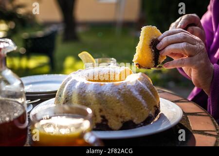 Serve una fetta di torta all'aperto. Torta di Pasqua e tè sul tavolo. Rinfresco nel giardino primaverile Foto Stock