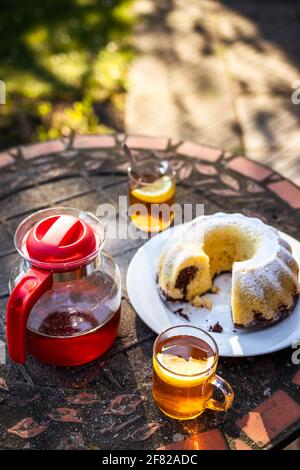 Picnic in primavera. Tè in tazza e teiera con torta in padella sul tavolo all'aperto. Serve dessert e bevande calde nel giardino di primavera Foto Stock