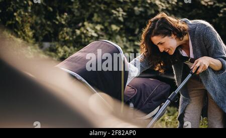Donna in congedo di maternità che prende il suo bambino fuori in un passeggino. Donna con baby pram all'aperto. Foto Stock
