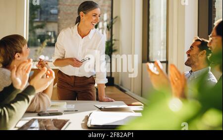 Felici membri del team che applaudono la guida per la sua guida nella pianificazione delle strategie. Felice donna che condivide il successo di startup in riunione Foto Stock