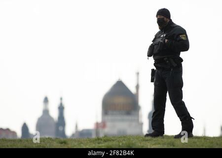11 aprile 2021, Sassonia, Dresda: Sullo sfondo della città vecchia, un poliziotto assicura l'ingresso a un parcheggio di fronte alla fiera. La conferenza dei partiti federali dell'AFD si terrà presso il centro fieristico dal 10 al 11 aprile 2021. Foto: Sebastian Kahnert/dpa-Zentralbild/dpa Foto Stock