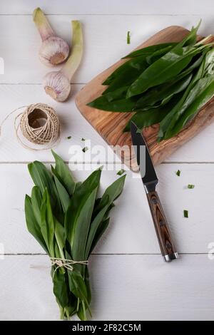 Aglio selvatico appena raccolto in un cesto di filo, impacchettato, con cesoie da giardino su tavola di legno bianco Foto Stock