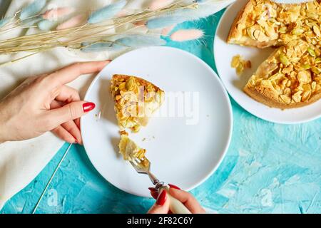 Le mani di donna irriconoscibile mangiano un pezzo di torta di mela o di pera con i dadi di caramello sul tavolo blu con luce solare, spazio di copia, vista dall'alto. Foto Stock