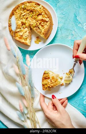 Le mani di donna irriconoscibile mangiano un pezzo di torta di mela o di pera con i dadi di caramello sul tavolo blu con luce solare, spazio di copia, vista dall'alto. Foto Stock