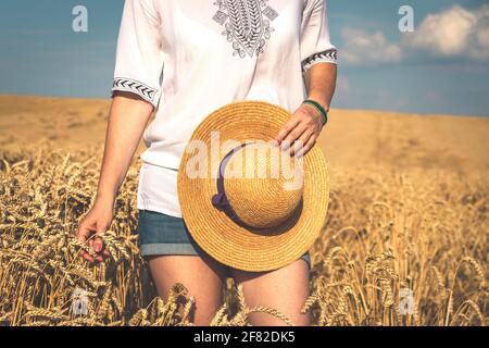 Donna che indossa abiti casual e che si gode l'estate sul campo. Donna che tiene il cappello di paglia in mano e che rimane nella scena rurale Foto Stock