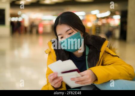 Donna asiatica che vola in covid19 volte - stile di vita ritratto di Giovane bella e stanca ragazza cinese in maschera in attesa in aeroporto con passaporto s Foto Stock