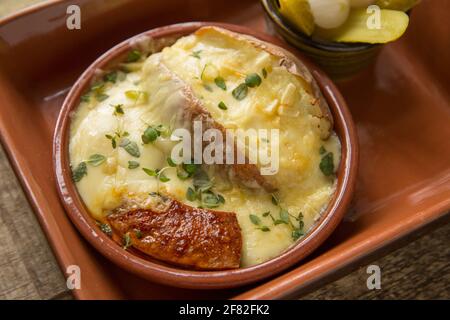 Un piatto fatto in casa di Raclette fuso, una patata al forno e salsiccia di chorizo alla griglia servita con cetriolini e cipolle sottaceto. Raclette ha avuto origine in Foto Stock