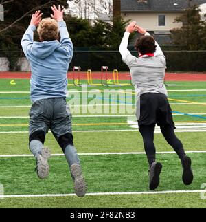 Due ragazzi a metà volo mentre saltano in pista e campo forza e agilità pratica su un campo erboso verde. Foto Stock