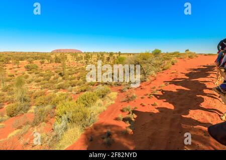 Uluru, Australia - Agosto 2019:ombra di persone sul cammello cavalcare nel deserto australiano del territorio del Nord con Uluru Ayers rock. Attività popolare a. Foto Stock