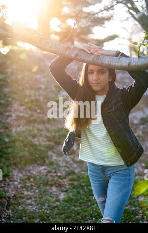 Ritratto all'aperto di una ragazza adolescente mista in un boschetto di ciliegi al tramonto in primavera. Foto Stock