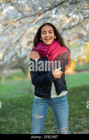 Ritratto all'aperto di una ragazza adolescente mista in un boschetto di ciliegi al tramonto in primavera. Foto Stock