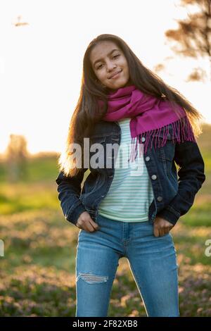 Ritratto all'aperto di una ragazza adolescente mista in un boschetto di ciliegi al tramonto in primavera. Foto Stock