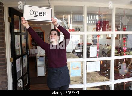 Harriet Henry, direttore della Tea Room di Knutsford, appende un cartello aperto fuori dal suo bar, mentre si prepara a dare il benvenuto ai clienti nella sua area salotto all'aperto, in quanto le restrizioni di blocco sono attenuate. Data immagine: Domenica 11 aprile 2021. Foto Stock