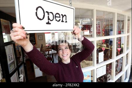 Harriet Henry, direttore della Tea Room di Knutsford, appende un cartello aperto fuori dal suo bar, mentre si prepara a dare il benvenuto ai clienti nella sua area salotto all'aperto, in quanto le restrizioni di blocco sono attenuate. Data immagine: Domenica 11 aprile 2021. Foto Stock