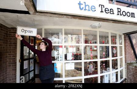 Harriet Henry, direttore della Tea Room di Knutsford, appende un cartello aperto fuori dal suo bar, mentre si prepara a dare il benvenuto ai clienti nella sua area salotto all'aperto, in quanto le restrizioni di blocco sono attenuate. Data immagine: Domenica 11 aprile 2021. Foto Stock