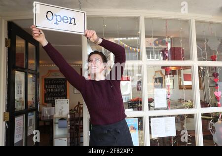 Harriet Henry, direttore della Tea Room di Knutsford, appende un cartello aperto fuori dal suo bar, mentre si prepara a dare il benvenuto ai clienti nella sua area salotto all'aperto, in quanto le restrizioni di blocco sono attenuate. Data immagine: Domenica 11 aprile 2021. Foto Stock