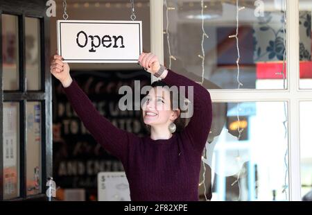 Harriet Henry, direttore della Tea Room di Knutsford, appende un cartello aperto fuori dal suo bar, mentre si prepara a dare il benvenuto ai clienti nella sua area salotto all'aperto, in quanto le restrizioni di blocco sono attenuate. Data immagine: Domenica 11 aprile 2021. Foto Stock