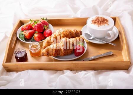vassoio per la colazione a letto : tazza di cappuccino, croissant e fragole fresche Foto Stock