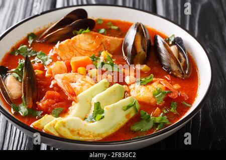 Deliziosa zuppa con frutti di mare, mais, sedano, pomodori, carote e avocado da vicino in una ciotola sul tavolo. Orizzontale Foto Stock