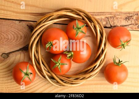 Diversi pomodori rossi biologici con una corona di vimini dalla vite, primo piano, su un tavolo di legno. Foto Stock