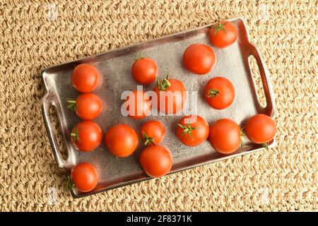 Diversi pomodori rossi maturi organici su un vassoio di metallo, primo piano, su un tappetino di paglia. Foto Stock