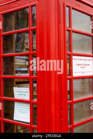Primo piano di una tradizionale scatola telefonica rossa ora in uso come scambio di libri della comunità locale nel villaggio di West End, Woking, Surrey Foto Stock