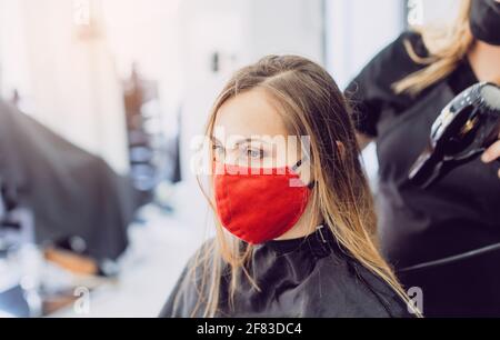Donna che indossa una maschera rossa per il viso che si sta facendo styling fresco in un parrucchiere Foto Stock