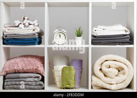 Organizzazione dello storage. Pile di asciugamani, lenzuola, lenzuola, coperte e cuscini su un ripiano bianco. Foto Stock