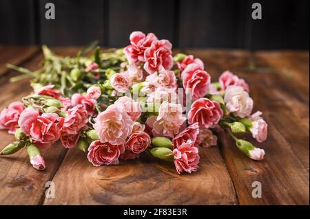 Bouquet di garofani rosa, bouquet di regali su sfondo ligneo. Concezione di cartoline con l'aggiunta di testo. Spazio di copia . Foto Stock