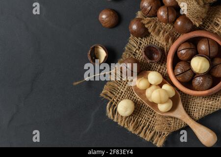 Noce di Macadamia arrosto secca in cucchiaio di legno e su fondo nero, le noci di Macadamia sono caricate con flavonoidi e tocotrienoli e ricchi di cuore sano Foto Stock