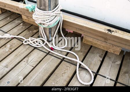 Primo piano di una corda nautica legata fino a a. posto di ormeggio su un molo di legno Foto Stock